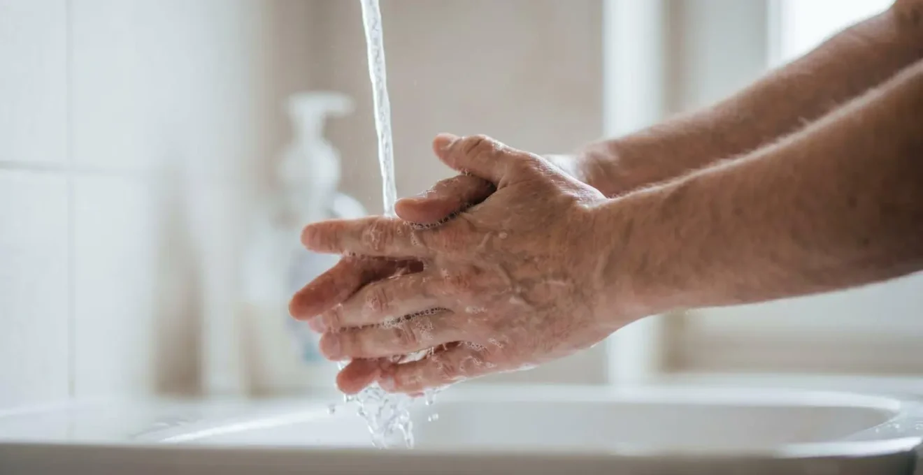 Human hands under running water with soap creating friction demonstrating proper handwashing technique